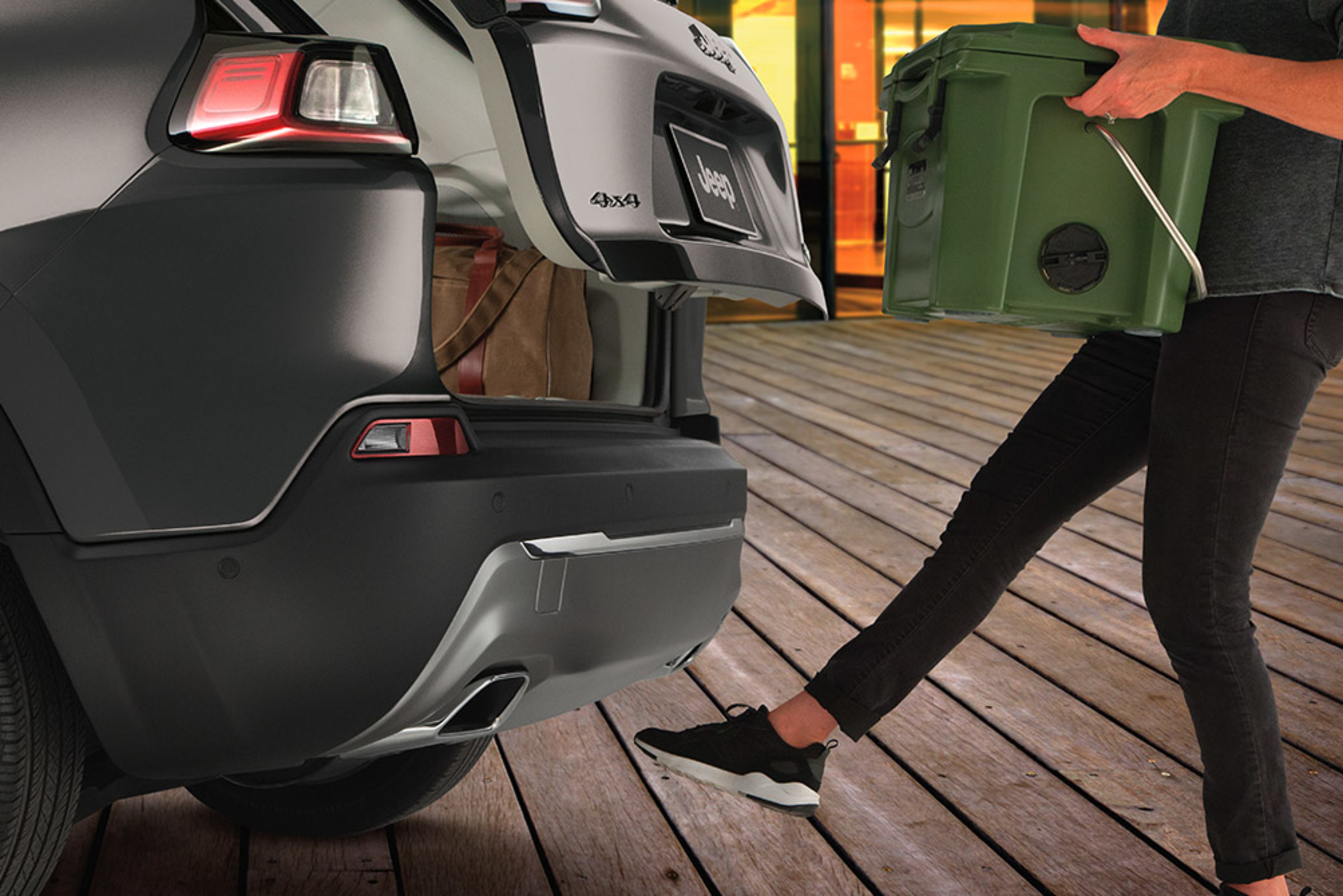 Close-up of the back of a grey 2021 Cherokee, with a man waving his foot below the rear bumber to open the rear with the available hands-free power liftgate.