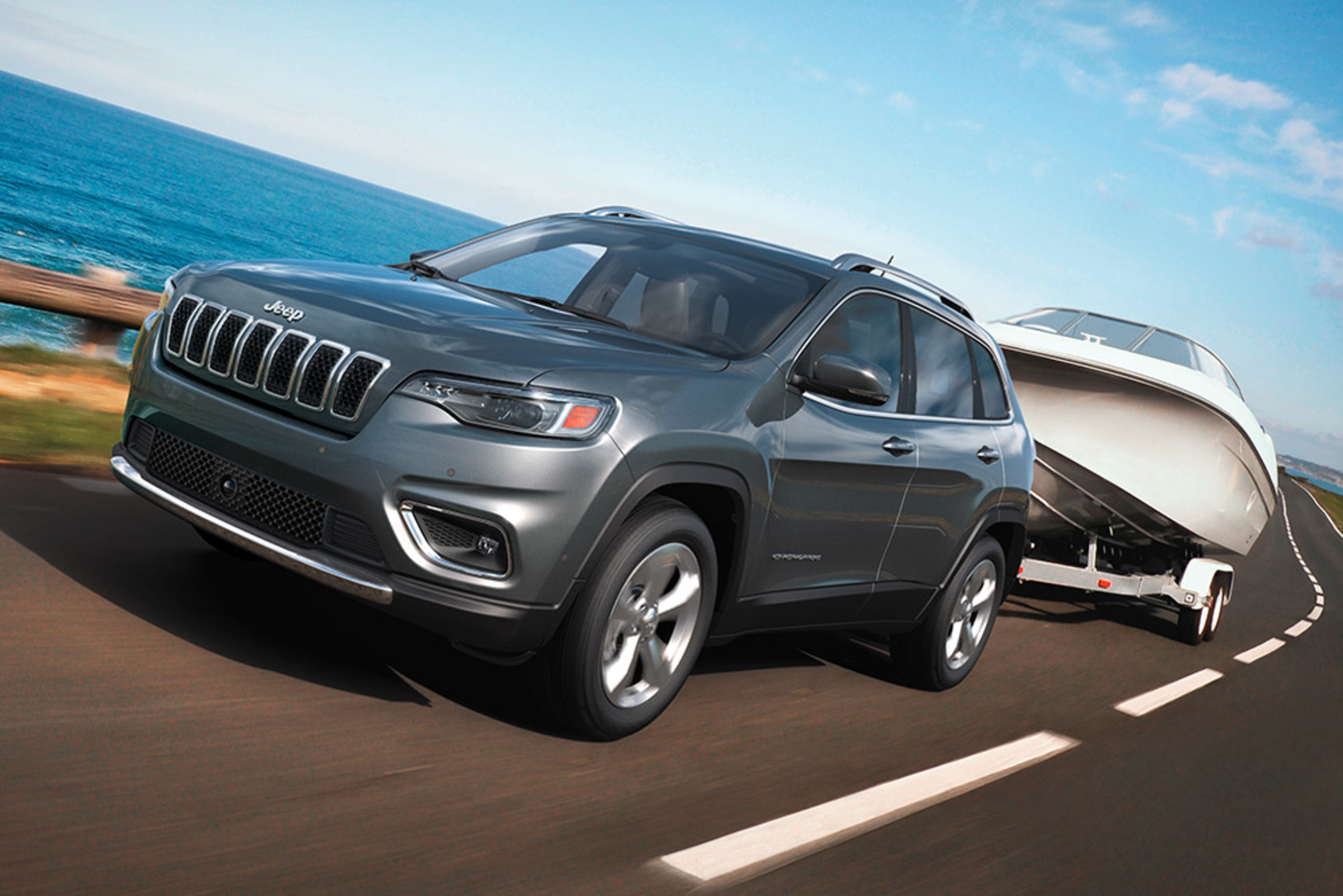2021 Jeep Cherokee towing a boat along a waterfront highway.