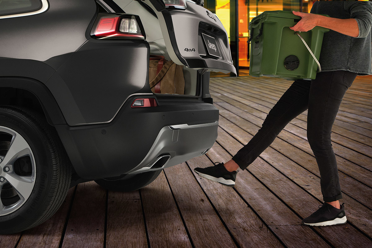 Woman using her foot to open the available hands-free power liftgate while holding a box in both hands.