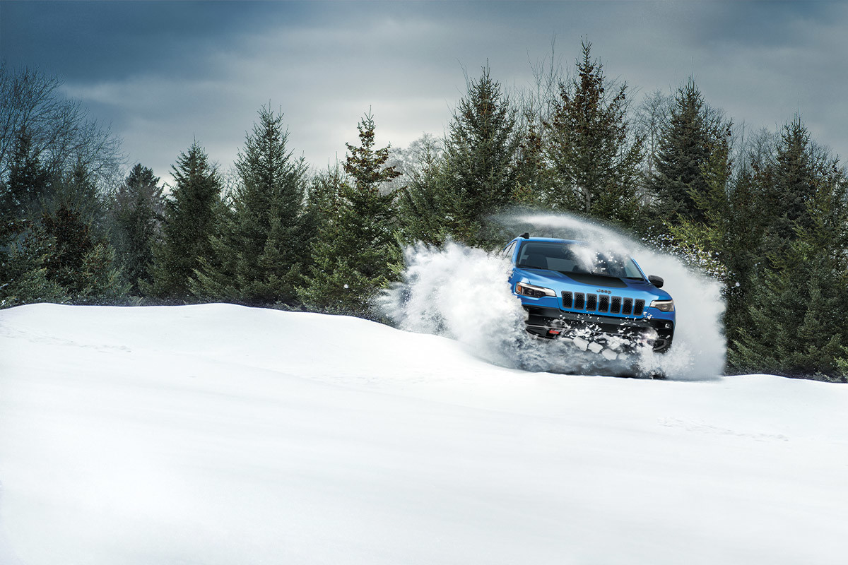 A 2022 Jeep Cherokee SUV driving on snow in a forest.