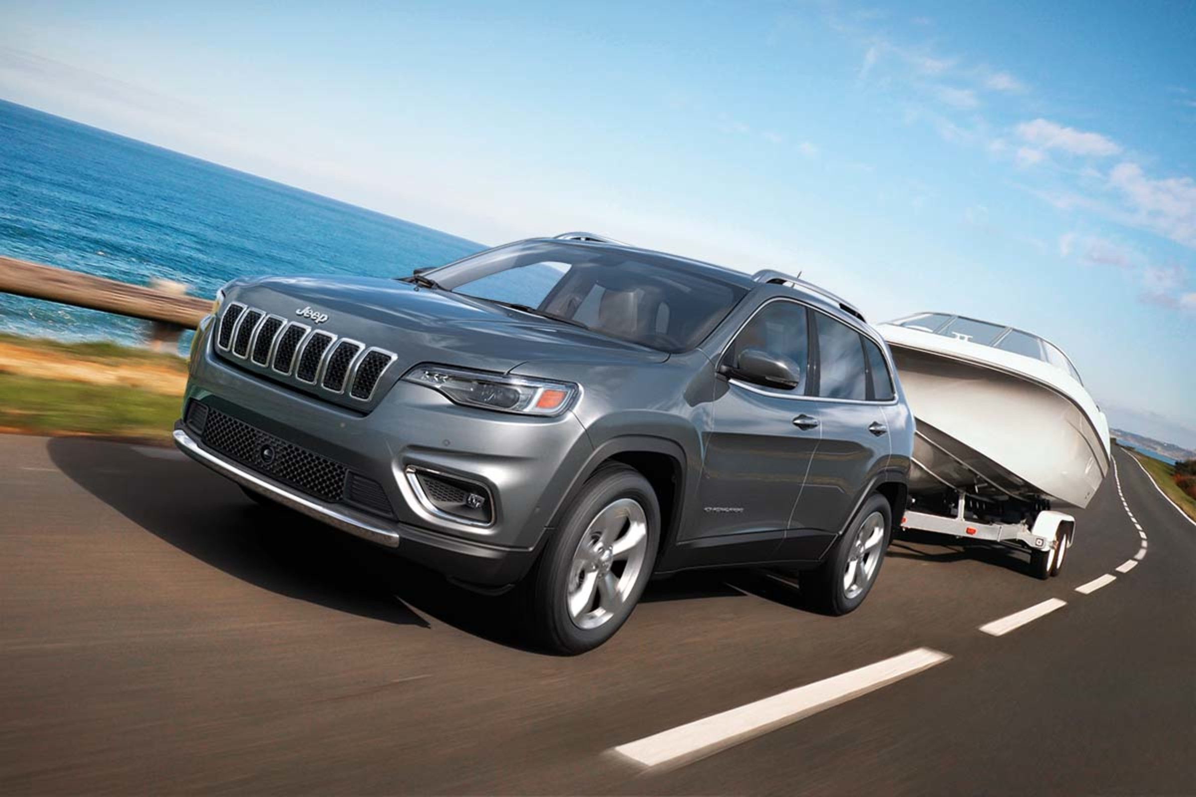 Front view of a 2022 Jeep Cherokee SUV towing a boat by a lake.