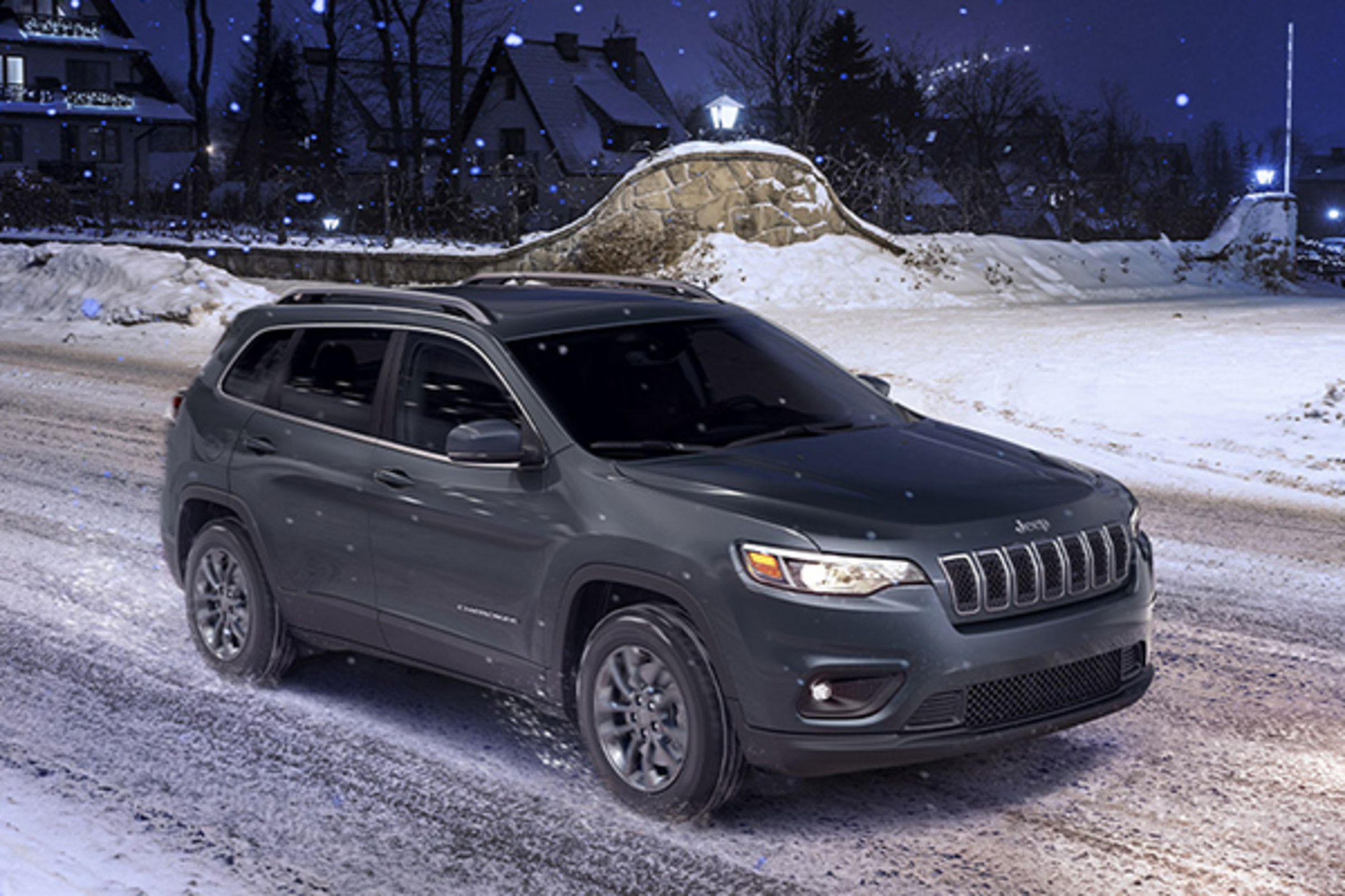 Side view of a gray Jeep Cherokee driving on a snowy road.