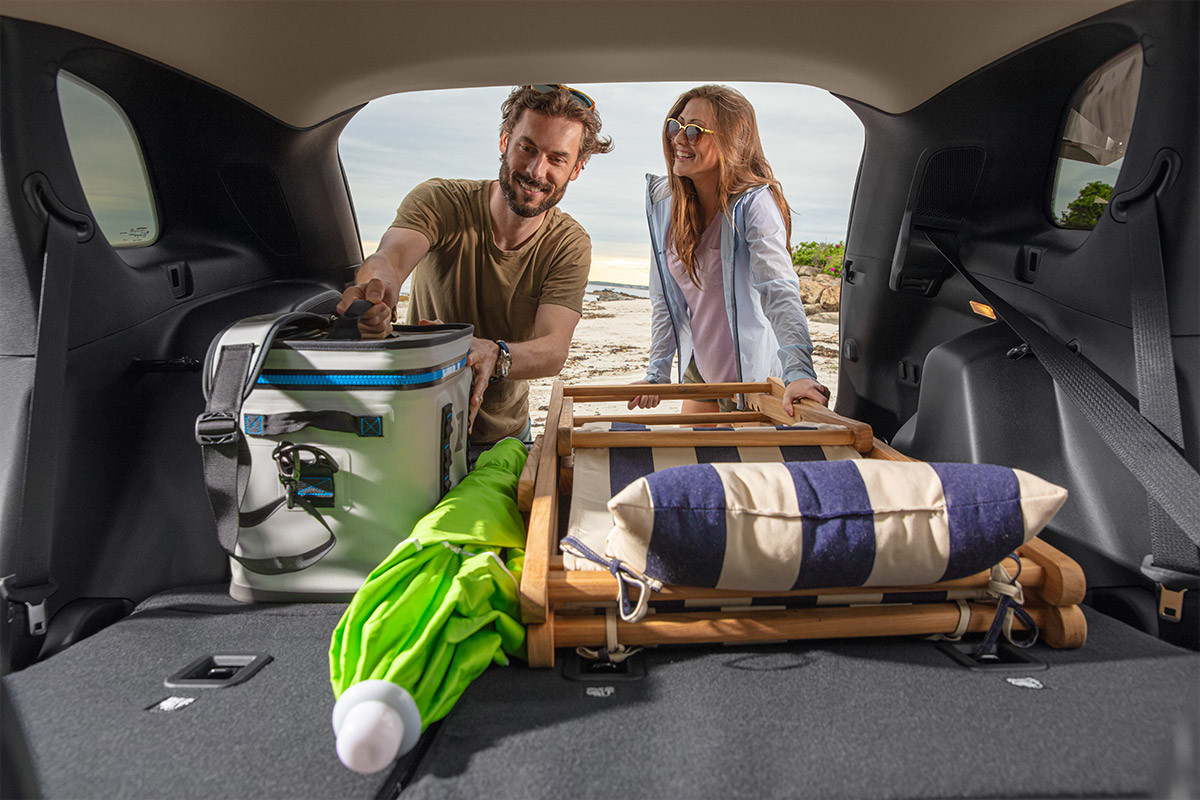 Happy couple at the beach, unloading folding chairs, a cooler and an umbrella from the back of a 2022 Jeep Cherokee SUV.