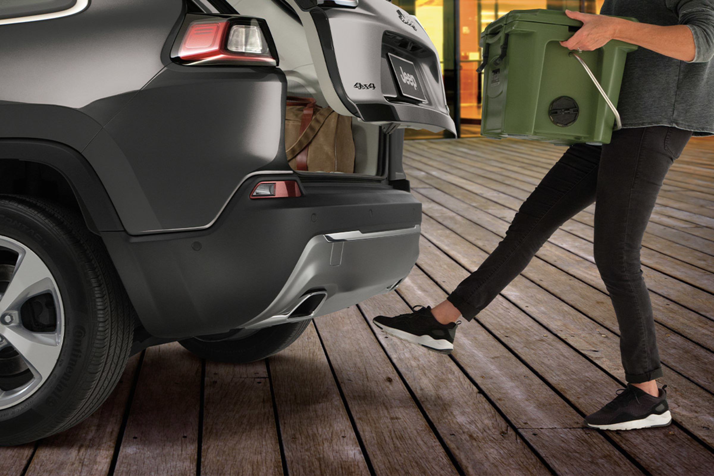 Woman using her foot to open the available hands-free power liftgate while holding a box in both hands.