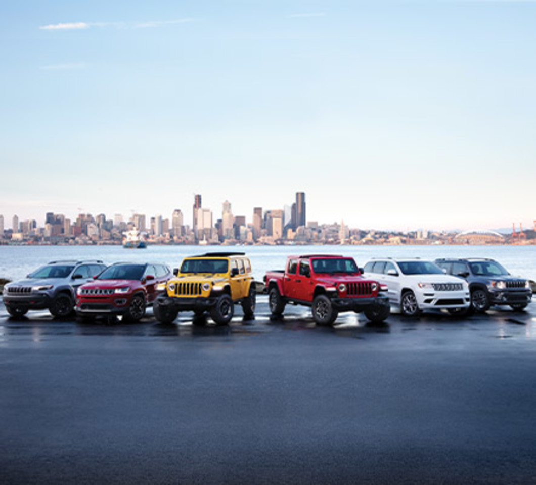 Lineup of front facing Jeep vehicles across a large body of water and city landscape.