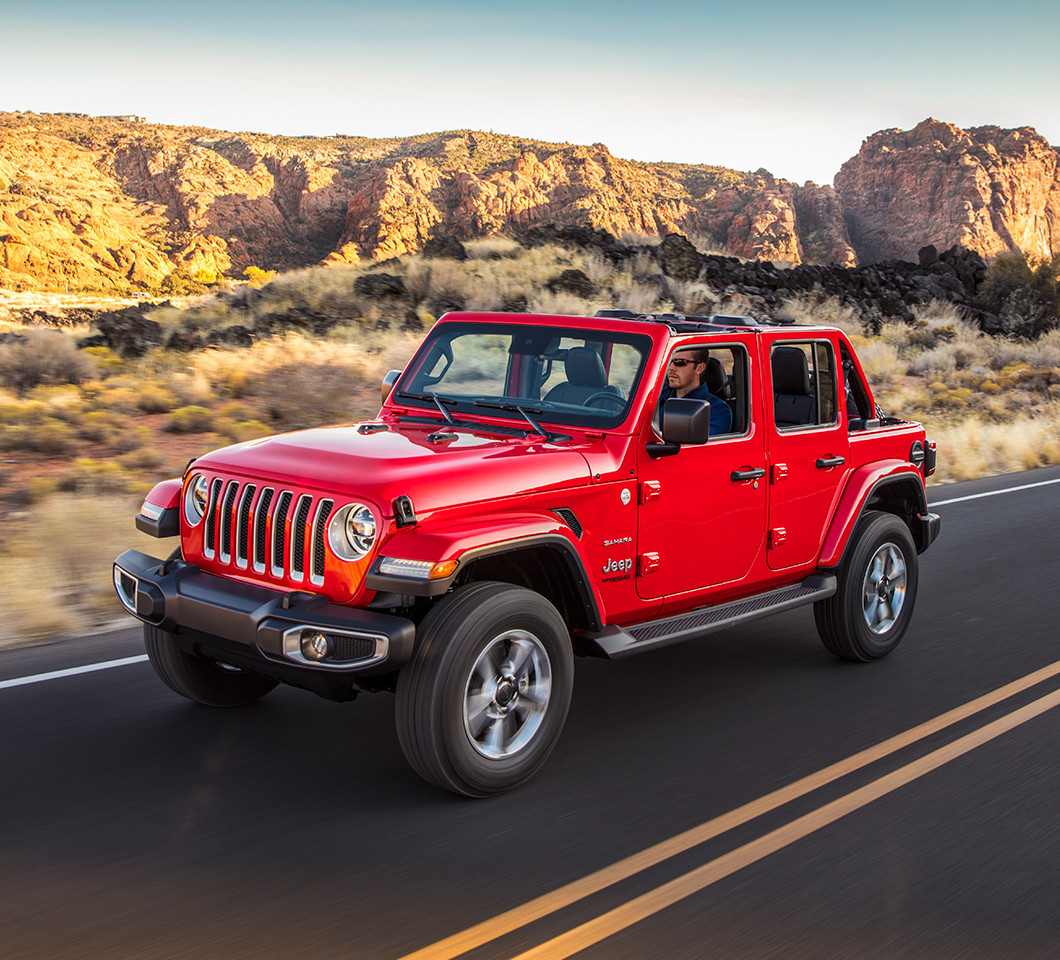 A side view of a red Jeep Wrangler driving on the road