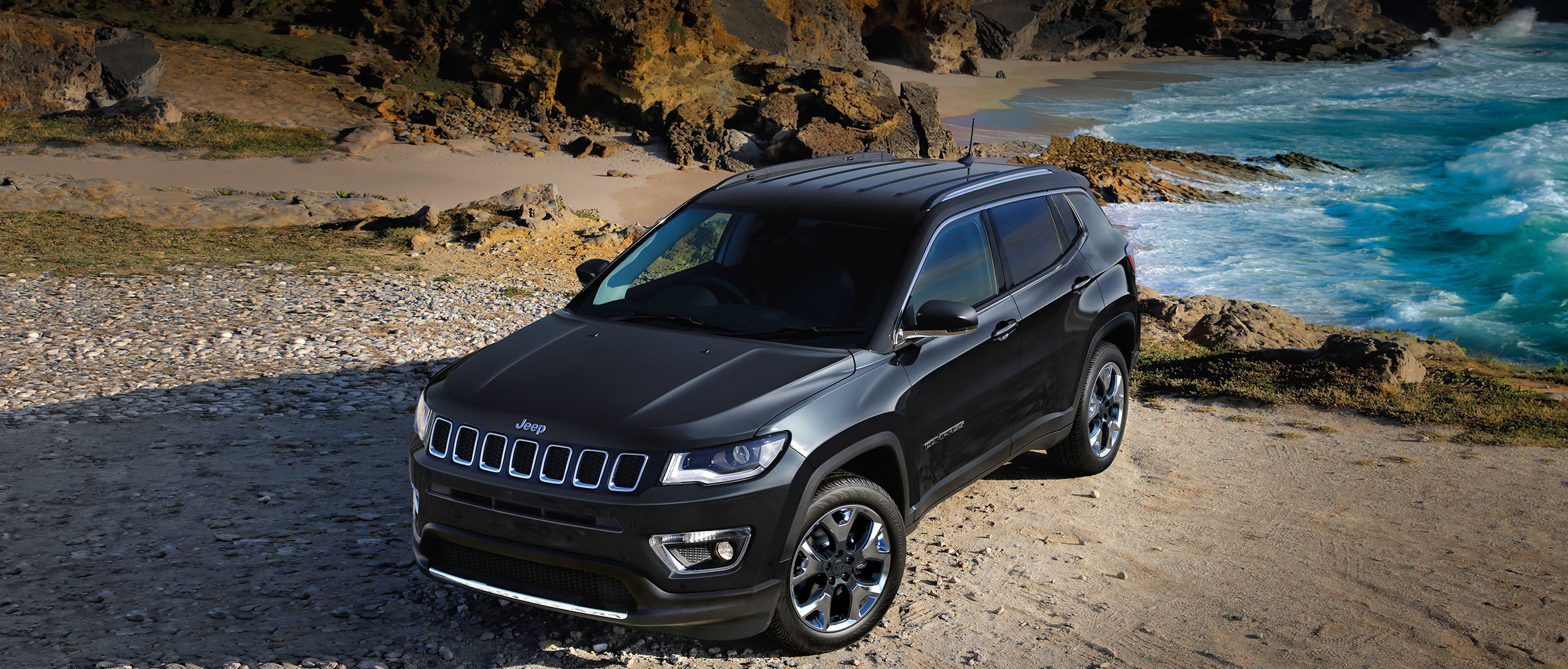 Black 2019 Jeep Compass, parked on a rocky beach.