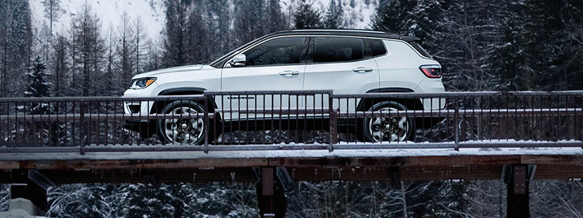 Vue latérale du Jeep Compass 2019, illustré en blanc, roulant sur un pont couvert de neige dans les montagnes