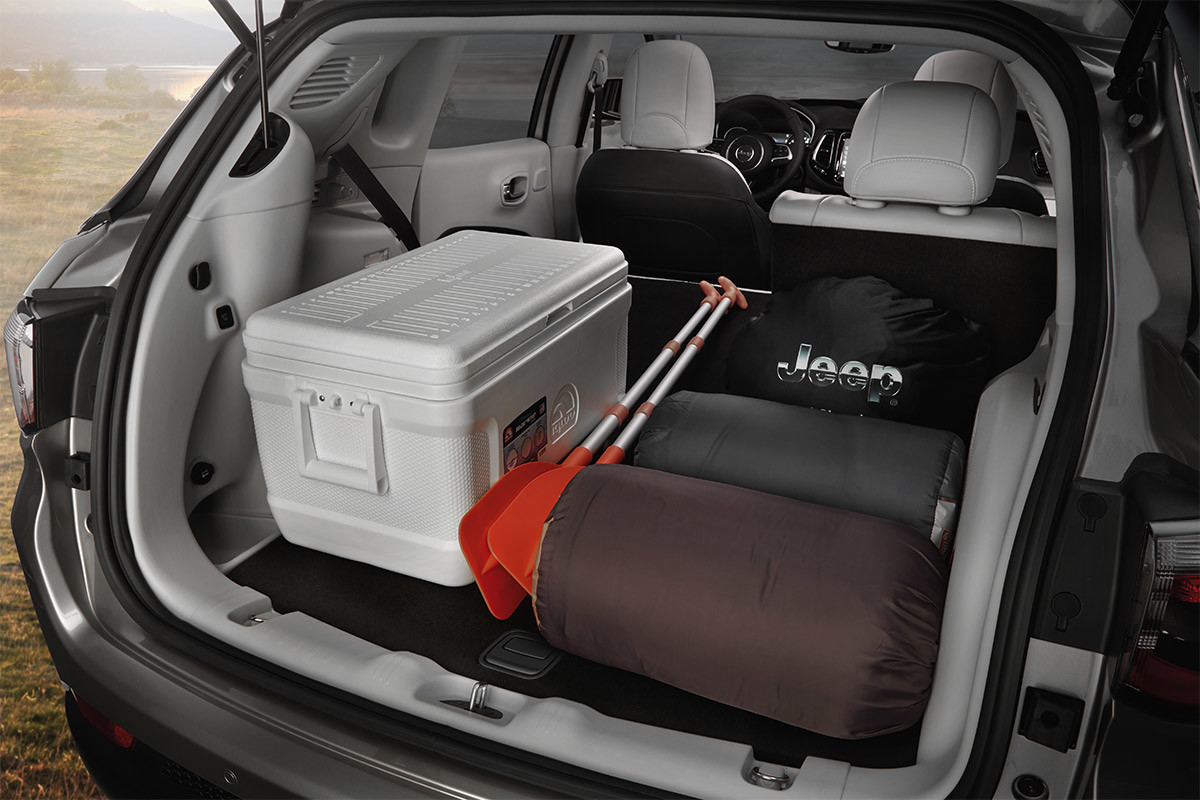 Open trunk of a 2020 Jeep Compass carrying 2 sleeping bags, kayak paddles, and a cooler.