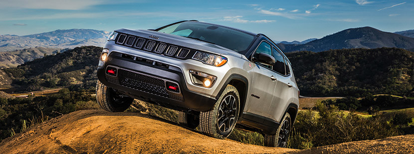 Silver 2020 Jeep Compass driving over hills by the mountains.
