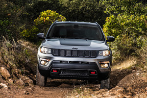 Jeep Compass de couleur argent avec garniture noire roulant sur un sentier rocailleux avec des arbres et des arbustes