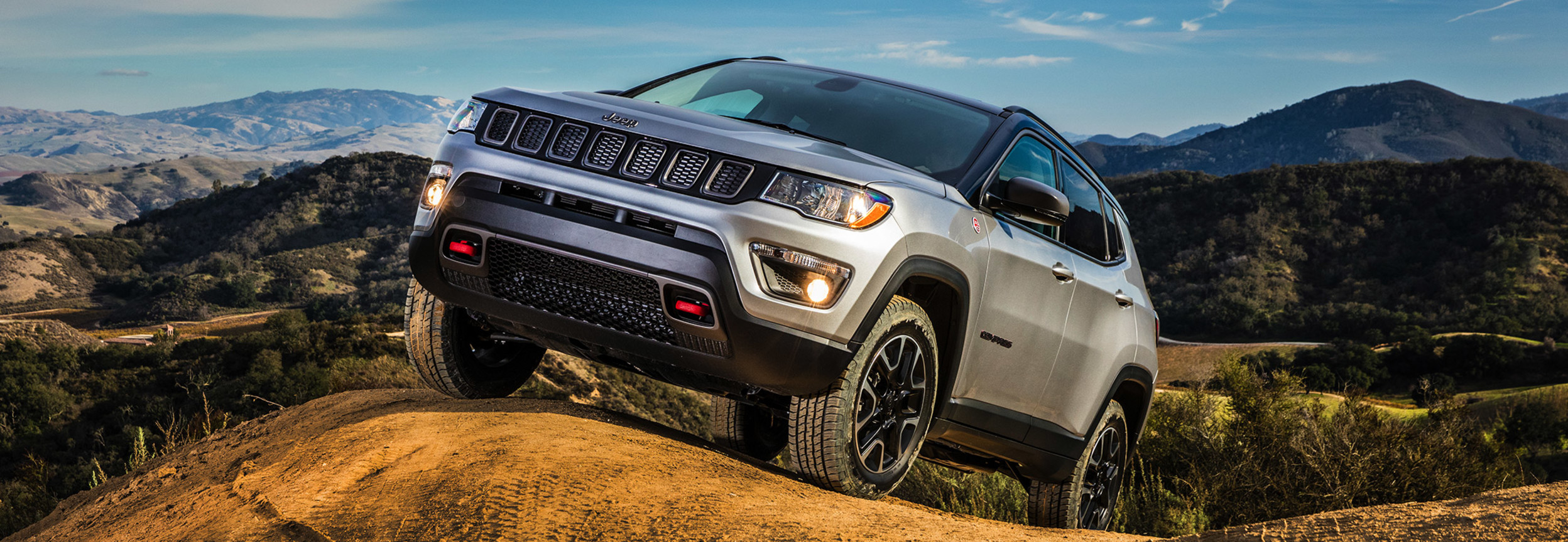 Silver Jeep Compass at a 45-degree angle, climbing up a hill.