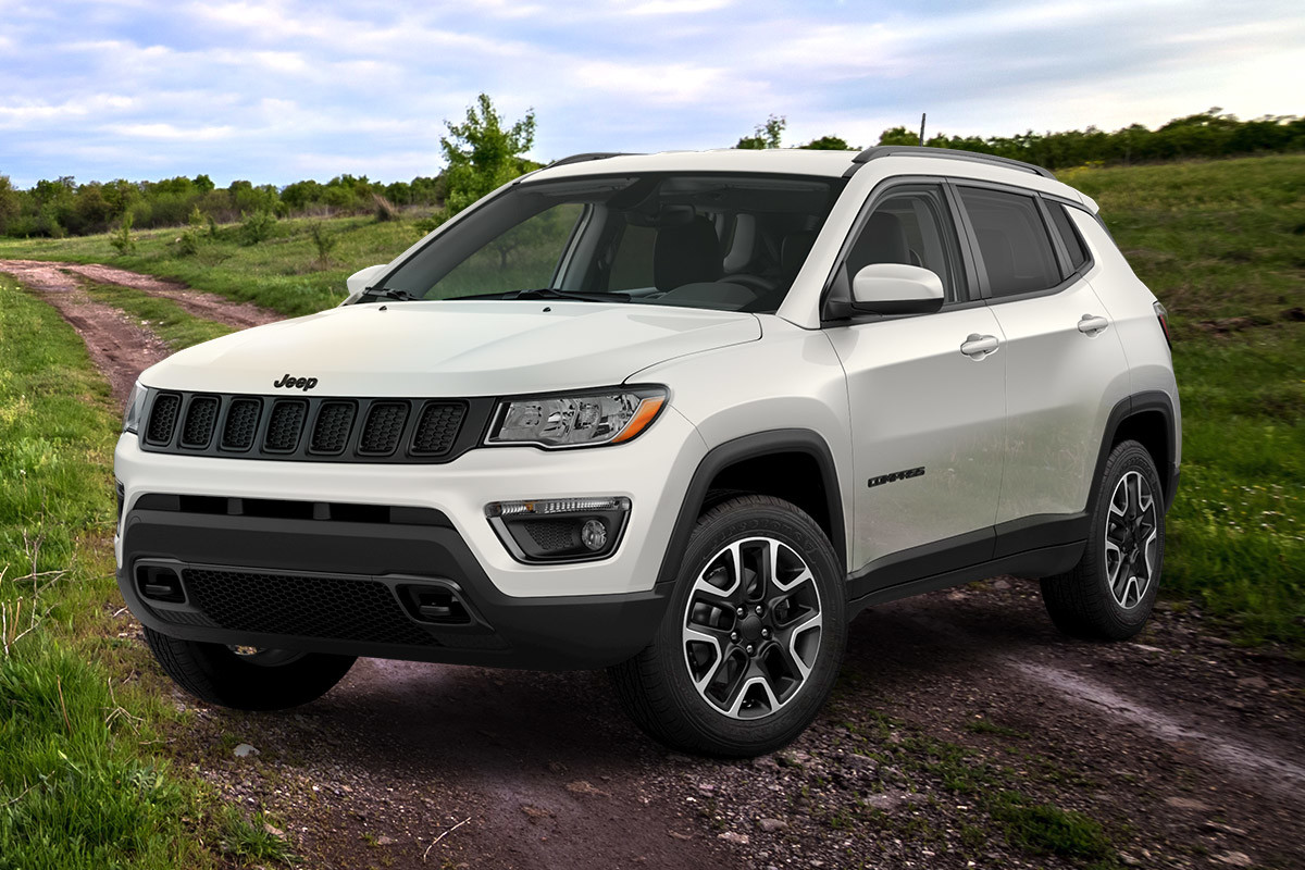 Jeep Compass blanc garé sur un chemin de terre avec un champ, des arbres et le ciel en arrière-plan.