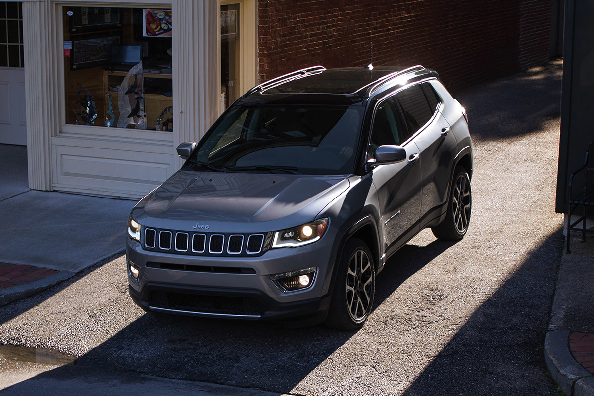 Jeep Compass de couleur argent sortant d’une ruelle pavée entre deux magasins.