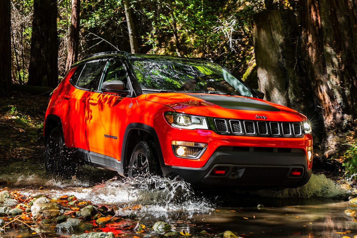 Red Jeep Compass off-roading through a rocky, watery path.