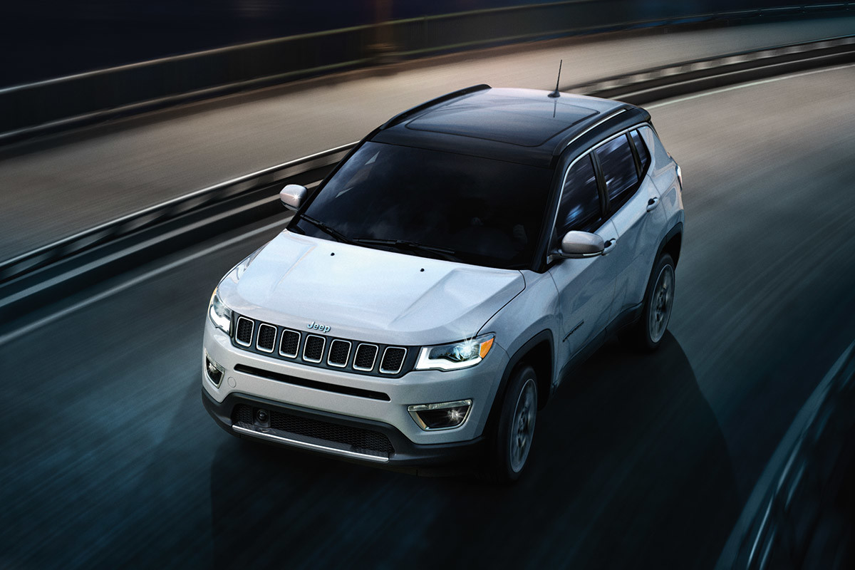 Jeep Compass blanc circulant sur une route pavée sinueuse divisée par un garde-corps en acier.