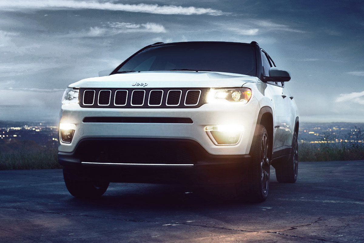 Jeep Compass blanc garé sur une route avec le crépuscule et les lumières de la ville en arrière-plan.