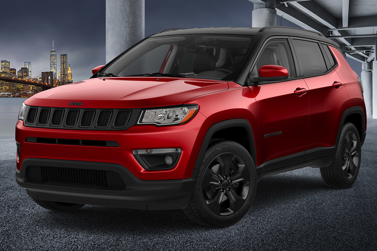 Jeep Compass rouge roulant sur un pont en béton la nuit avec une ville en arrière-plan.