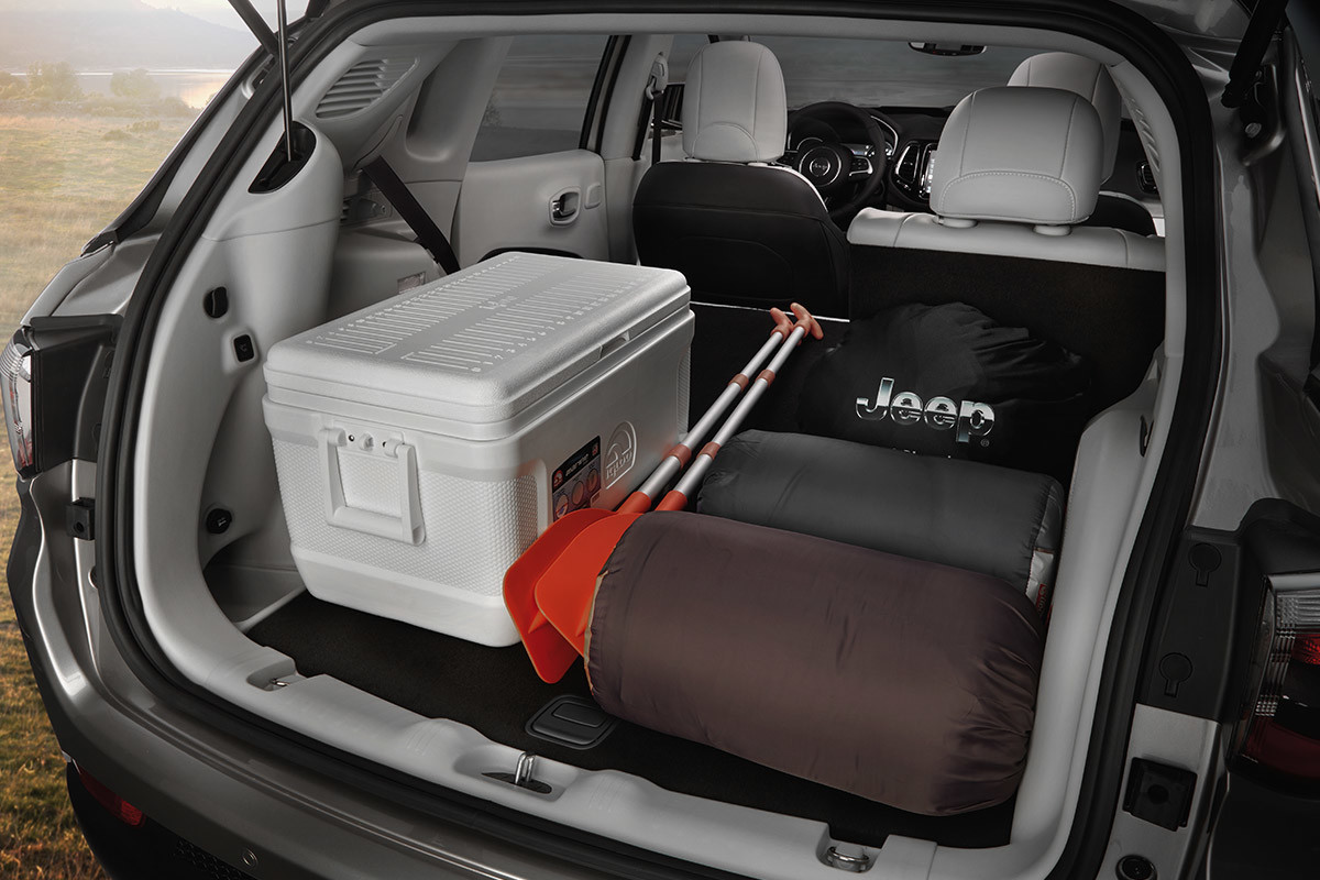 Coffre ouvert d’un Jeep Compass transportant deux sacs de couchage, des pagaies de kayak et une glacière.