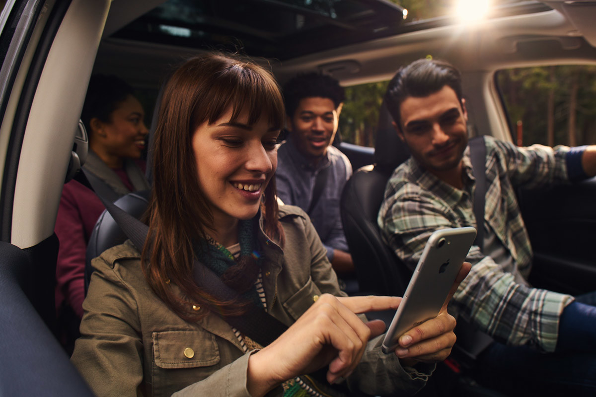Four passengers looking at a woman touching her smartphone in the front passenger seat.