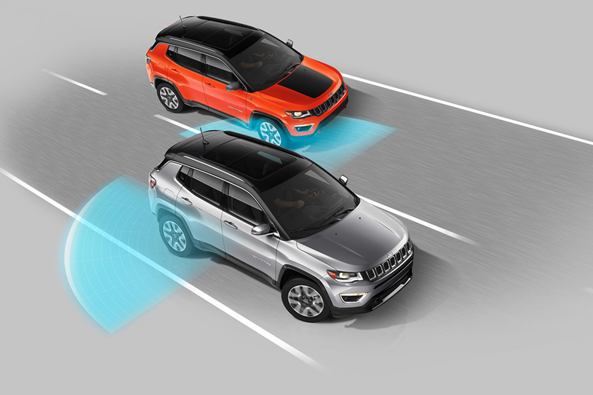 Vue aérienne d'un Jeep Compass Trailhawk 2021 de couleur orange dans l'angle mort d'un Jeep Compass 2021 de couleur argentée. Des capteurs bleus illustrés représentant les systèmes de surveillance des angles morts disponibles émanent des côtés arrière du véhicule argenté.