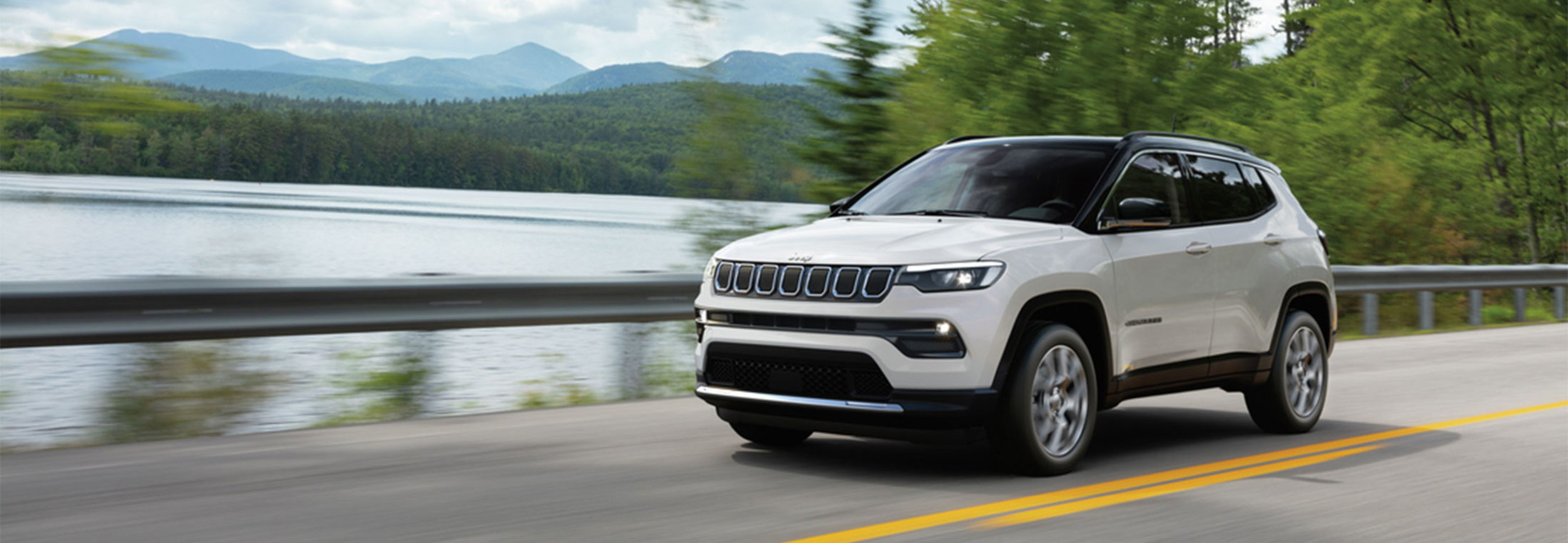 Jeep Compass blanche roulant le long d'un lac.
