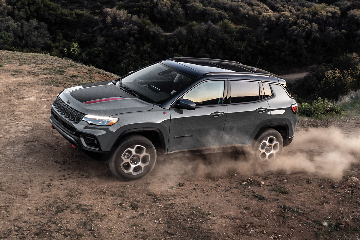 A grey 2022 Jeep Compass driving uphill on a dirt road.