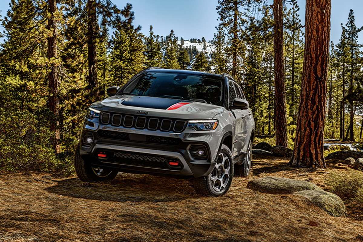 COMPÉTENCES ET EXCELLENCE L'avant d'un Jeep Compass 2022 gris garé dans une forêt.