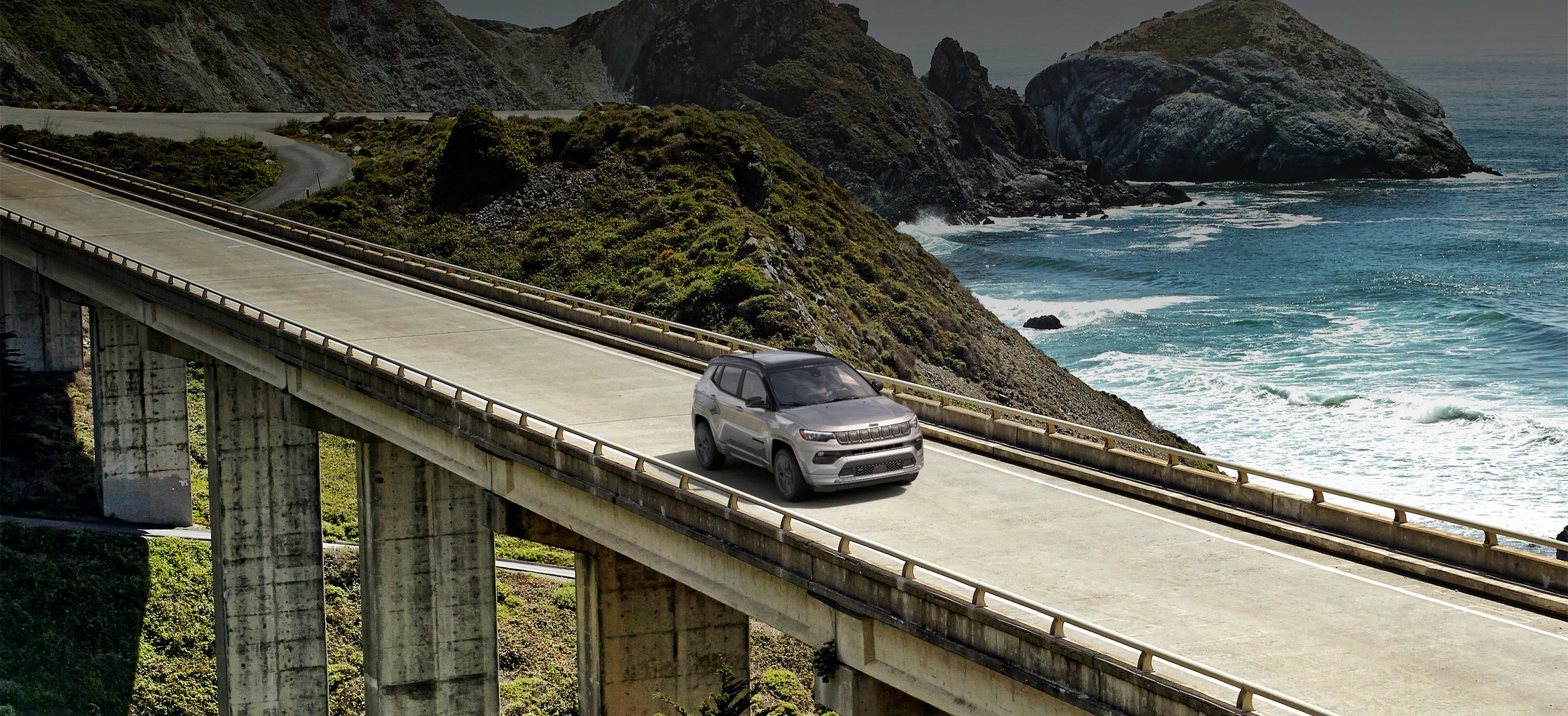 Vue aérienne du Jeep Compass 2022 redessiné roulant sur un pont au-dessus d’une étendue d’eau.