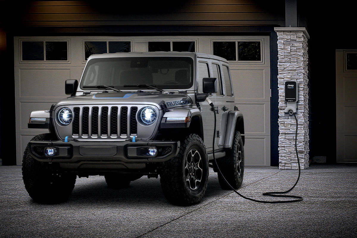 Vue d’un Jeep Rubicon 2023 gris en train d’être rechargé à l’extérieur d’un garage, la nuit.