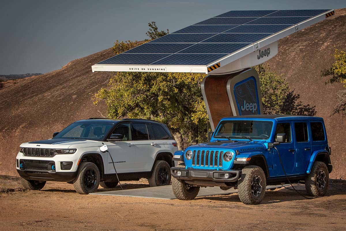 Vue de deux modèles Jeep VE stationnés sous une borne de recharge avec un terrain désertique en arrière-plan.