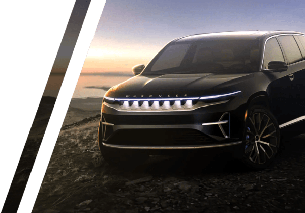 View of a black 2023 Jeep Wagoneer S model parked on top of a gravel path with water and sunrise in the background.
