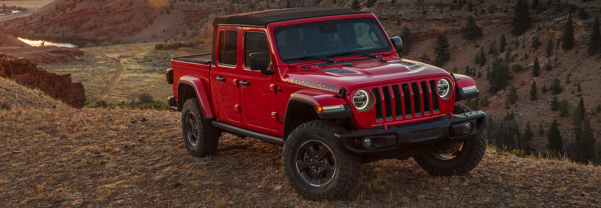 Vue latérale d’un Jeep Gladiator rouge stationné en haut d’une falaise avec des montagnes en arrière-plan