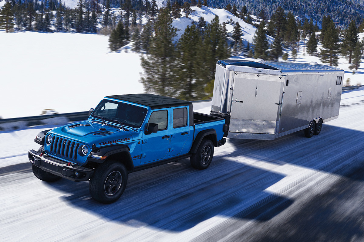 Front view of the all-new 2020 Jeep Gladiator Rubicon in blue driving on a snow-covered road while towing a trailer