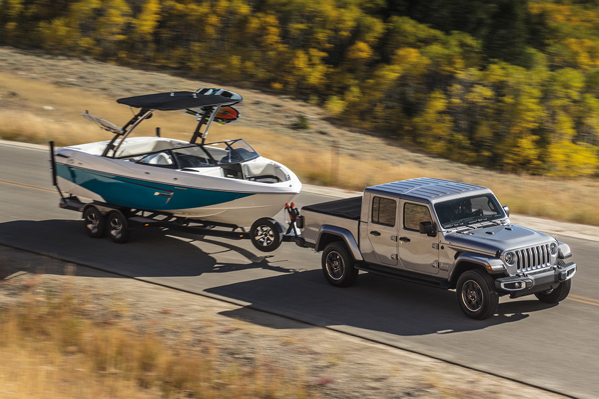 Jeep Gladiator 2020 argent remorquant un bateau blanc et bleu dans une plaine dans la forêt avec un lac en arrière-plan.