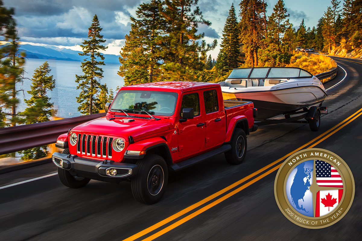 A red 2020 Jeep Gladiator, the winner of the 2020 North American Truck of The Year, towing a boat down a road by a lake