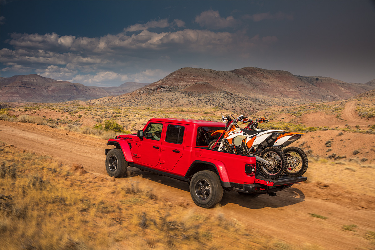 Vue arrière du Jeep Gladiator 2020, illustré en rouge, roulant sur une route de terre avec des motocyclettes dans l’espace utilitaire