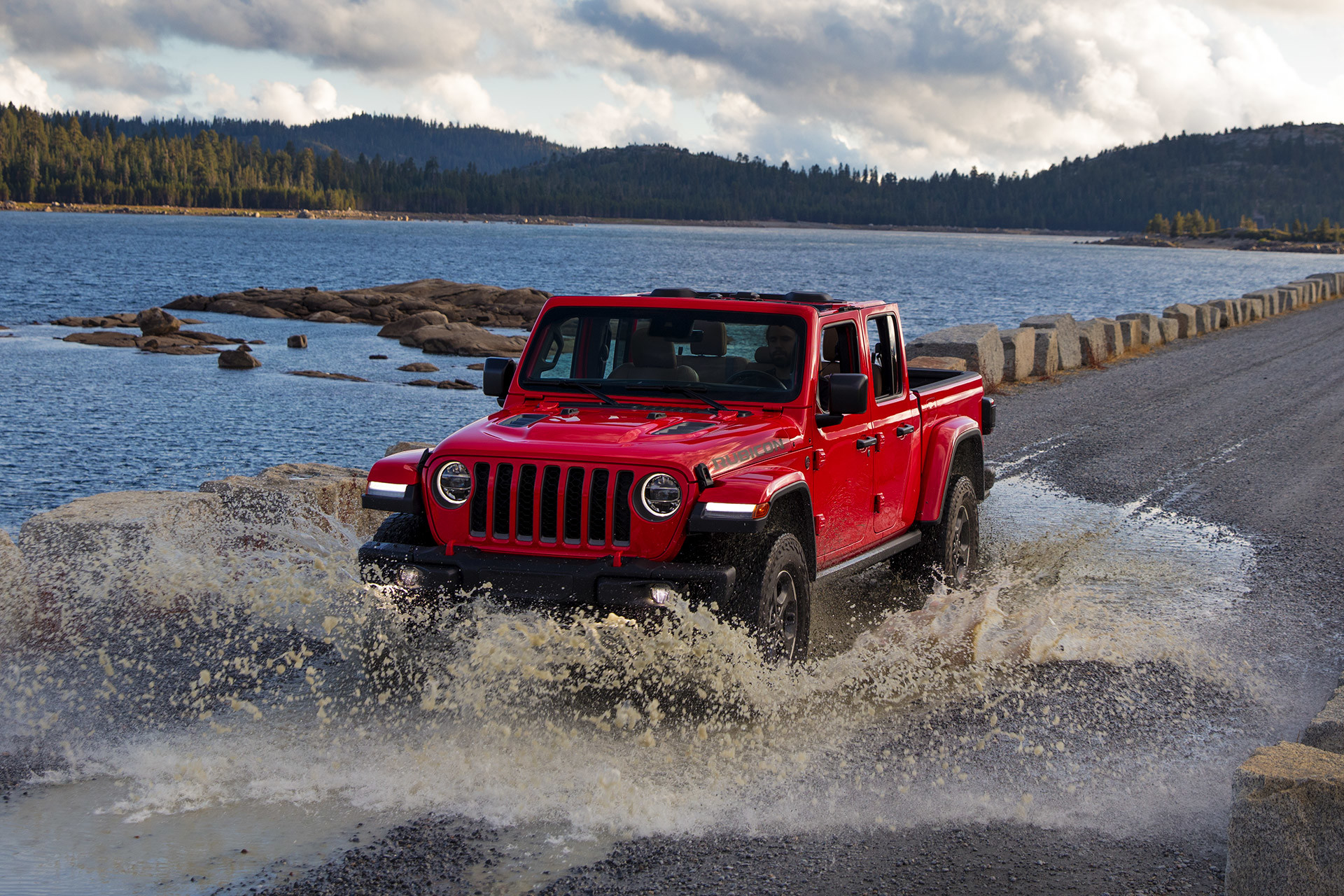 Jeep Gladiator 2020 rouge franchissant une grande flaque d’eau sur une route de gravier.