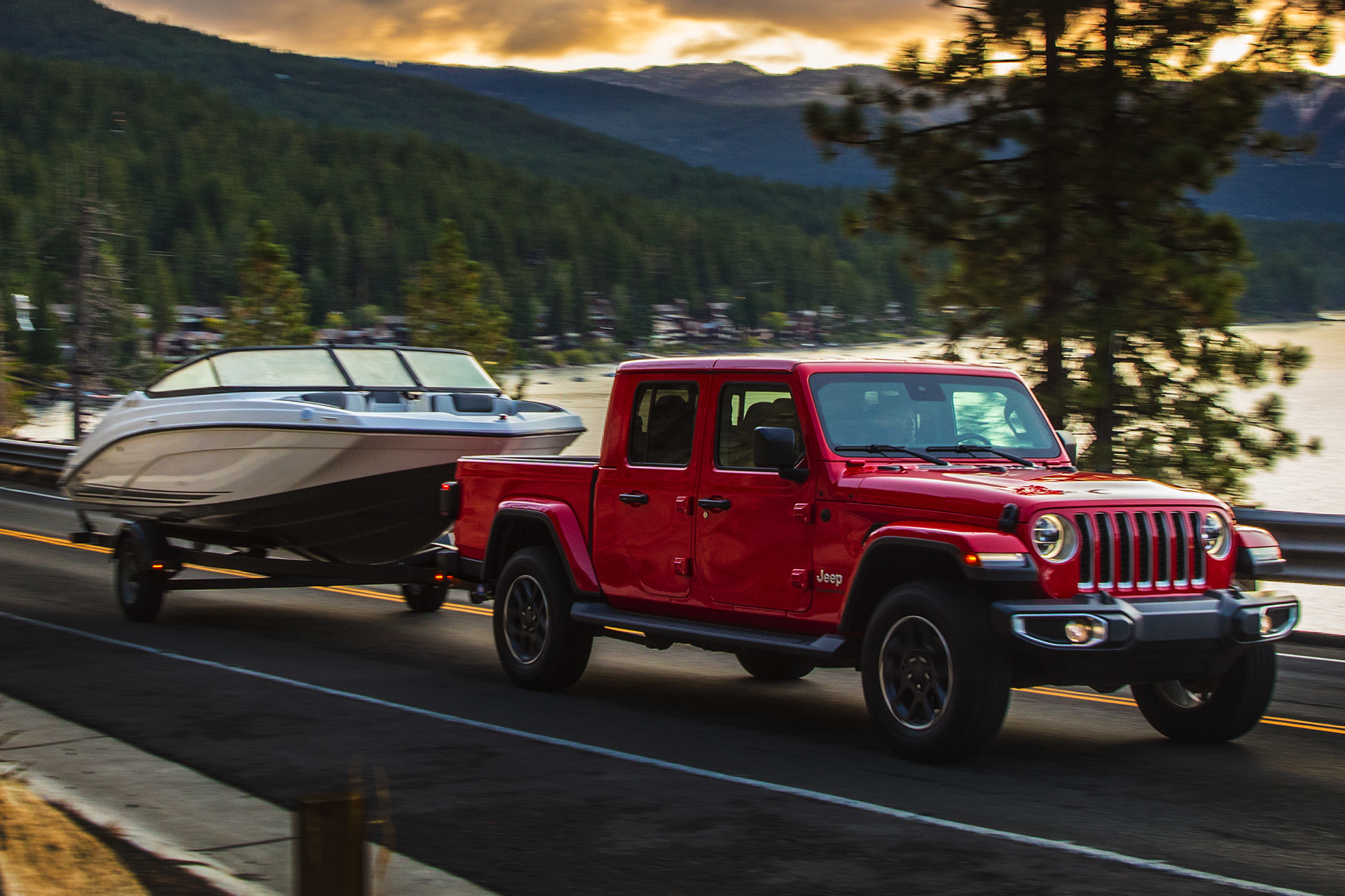 Jeep Gladiator 2020 rouge remorquant un bateau blanc dans les montagnes avec un lac en arrière-plan.