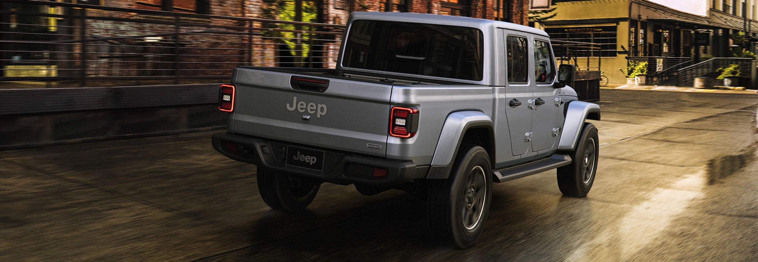 Vue arrière d’un Jeep Gladiator de couleur argent roulant dans une rue de la ville.