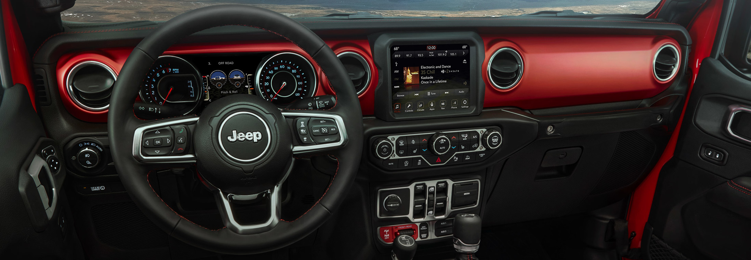 Habitacle du Jeep Gladiator du point de vue du conducteur, y compris le volant et le centre multimédia Uconnect, avec des montagnes visibles à travers le pare-brise.