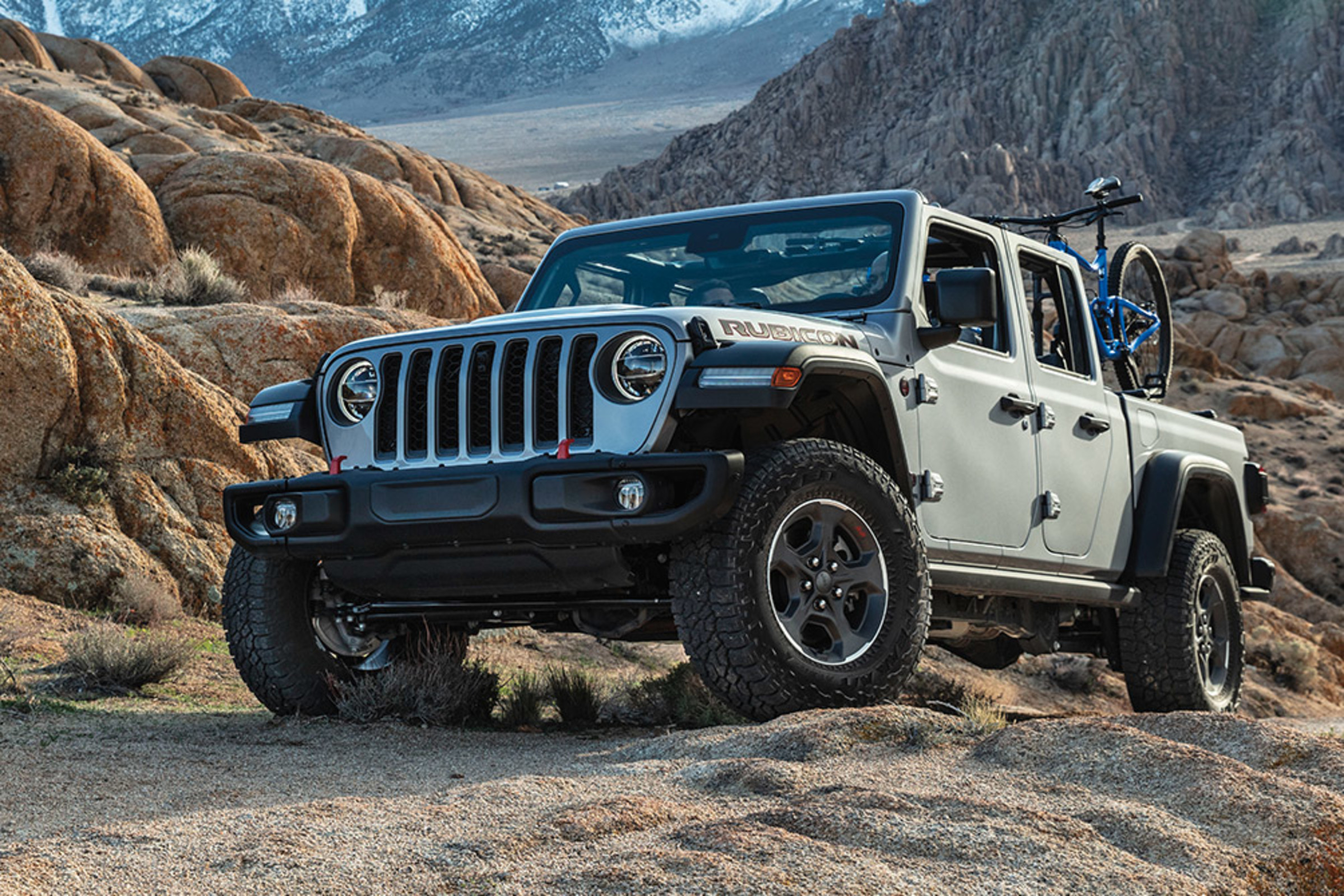 Vue avant d’un Jeep Gladiator Rubicon 2021 gris acier argenté métallisé garé sur une pente dans le désert avec des montagnes en arrière-plan. Un vélo est monté dans la plateforme du véhicule.