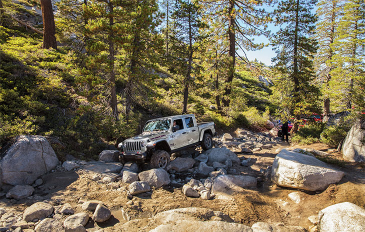 Side view of a grey Jeep Gladiator being driven on stones.