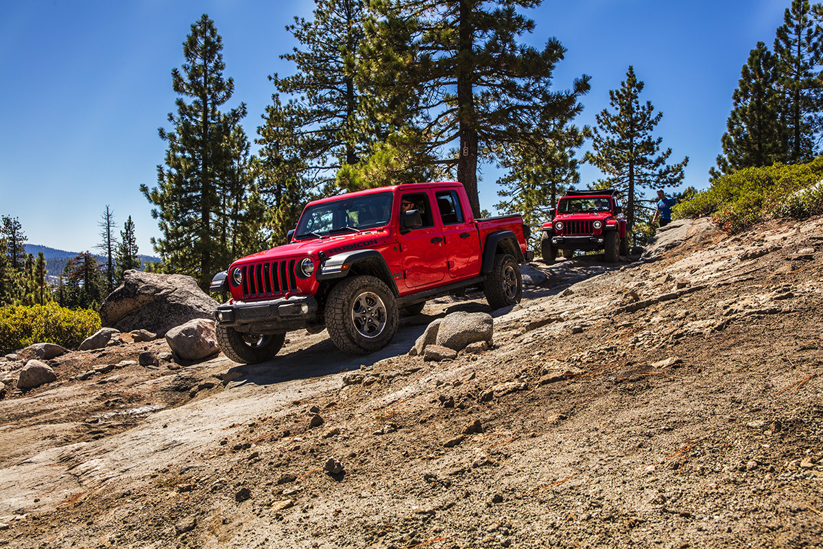 Two red Jeep Gladiator Rubicon vehicles driving one after another down a rocky off-road trail.