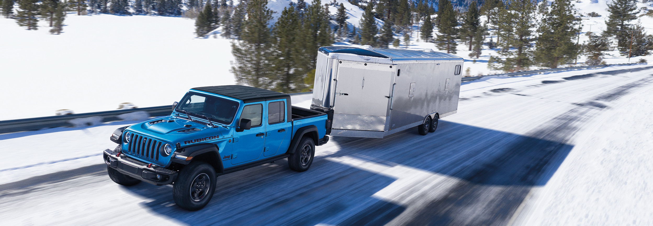 A blue 2022 Jeep Gladiator towing a large trailer on a snowy road.