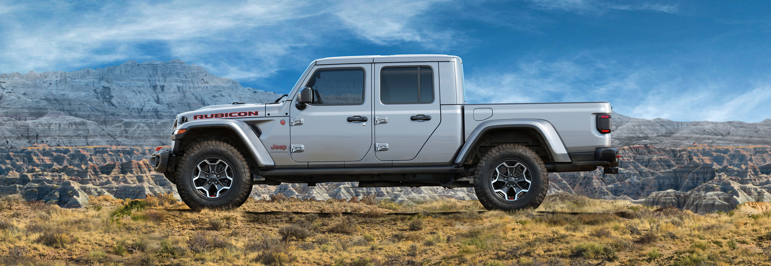 Side view of a light grey 2022 Jeep Gladiator with a mountain filled background.