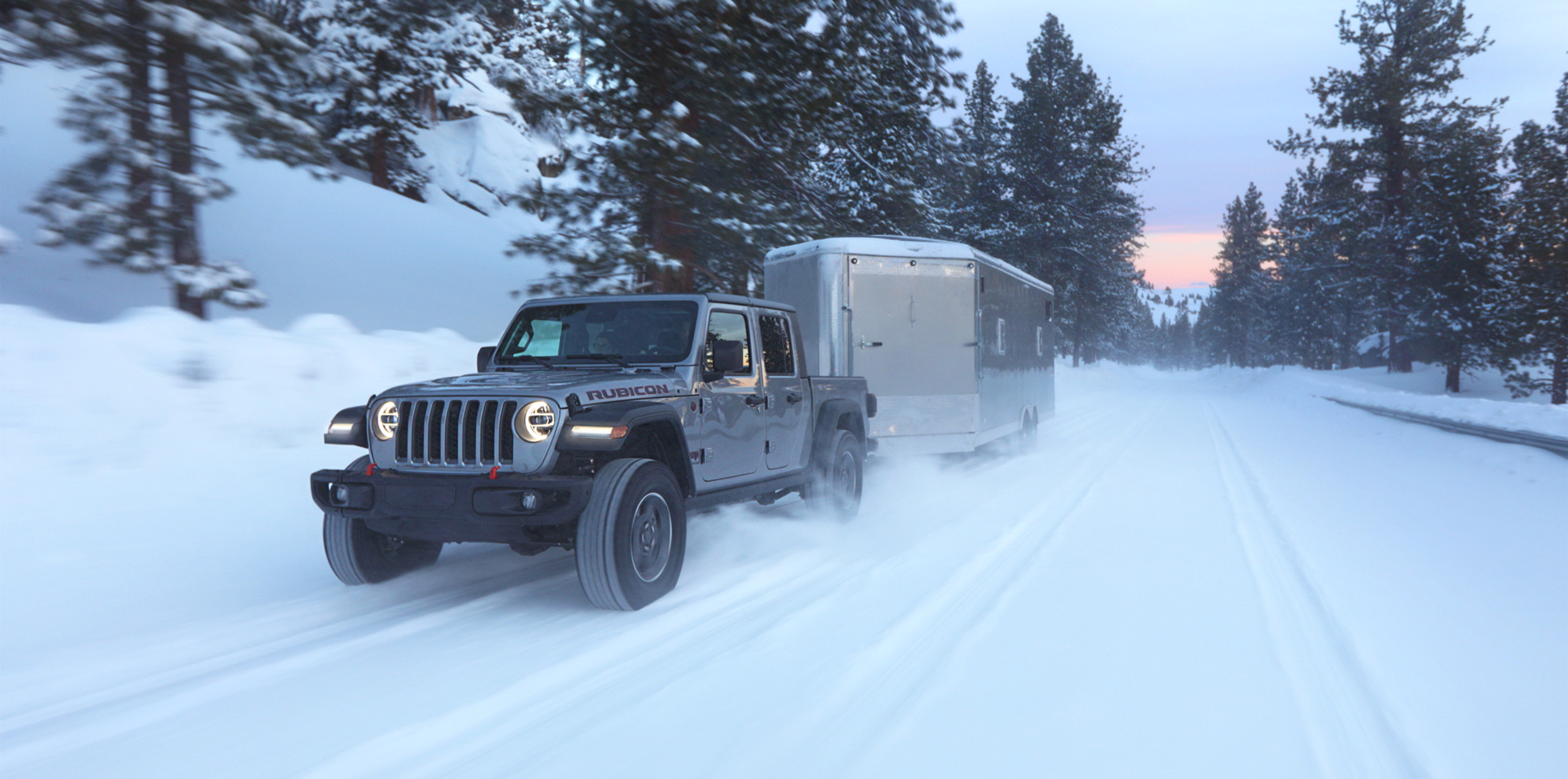Un Jeep Gladiator 2022 gris tirant une grande remorque dans la neige.