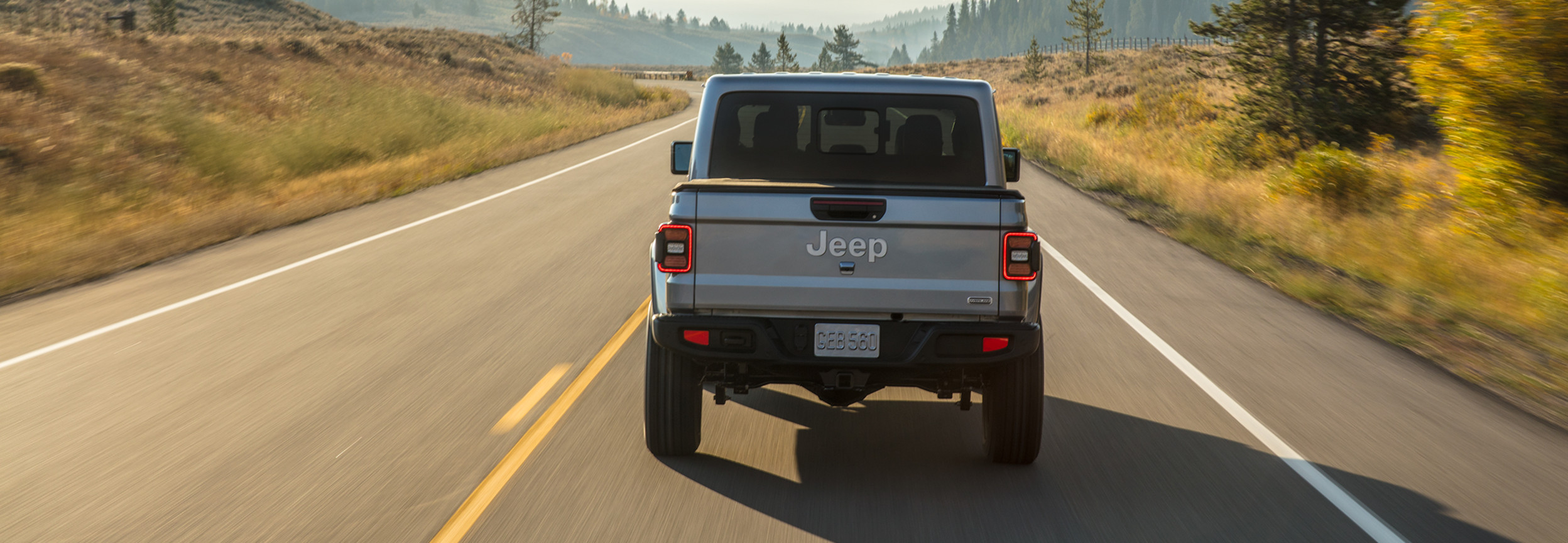 The back of a light grey 2022 Jeep Gladiator driving down a highway.
