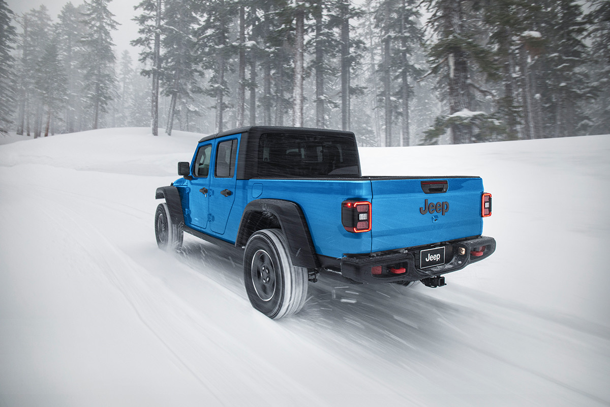 The back of a light blue Jeep Gladiator driving through the snow.
