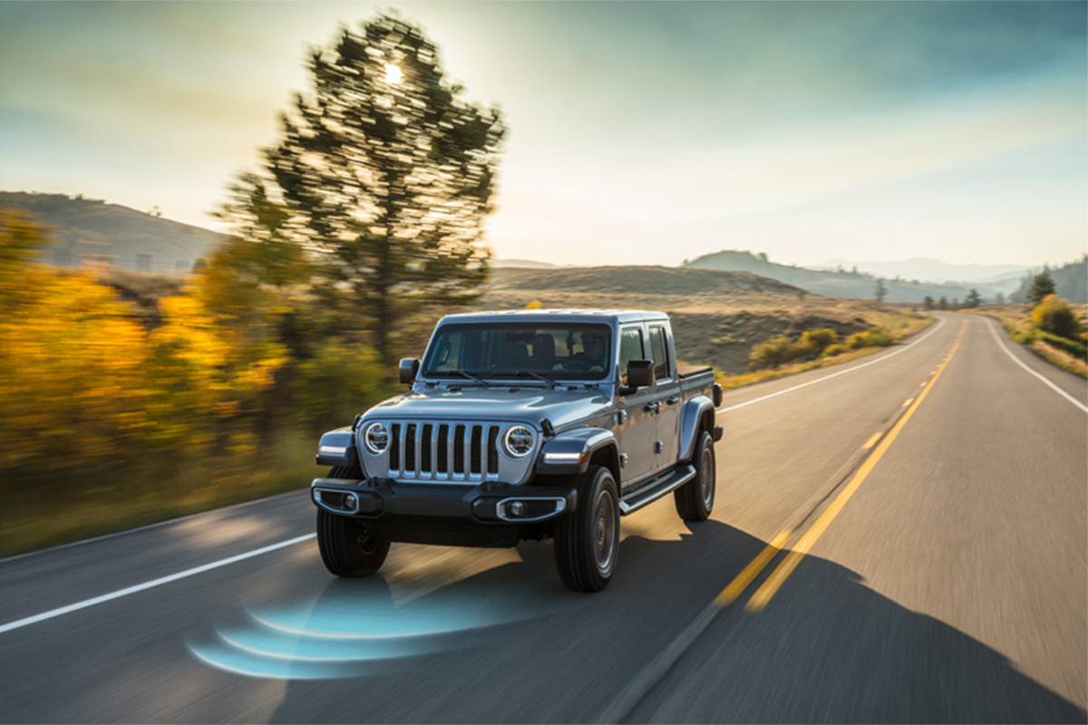 The front of a 2022 Jeep Gladiator driving down a highway with a blue radar in front of it to show off the adaptive cruise control.